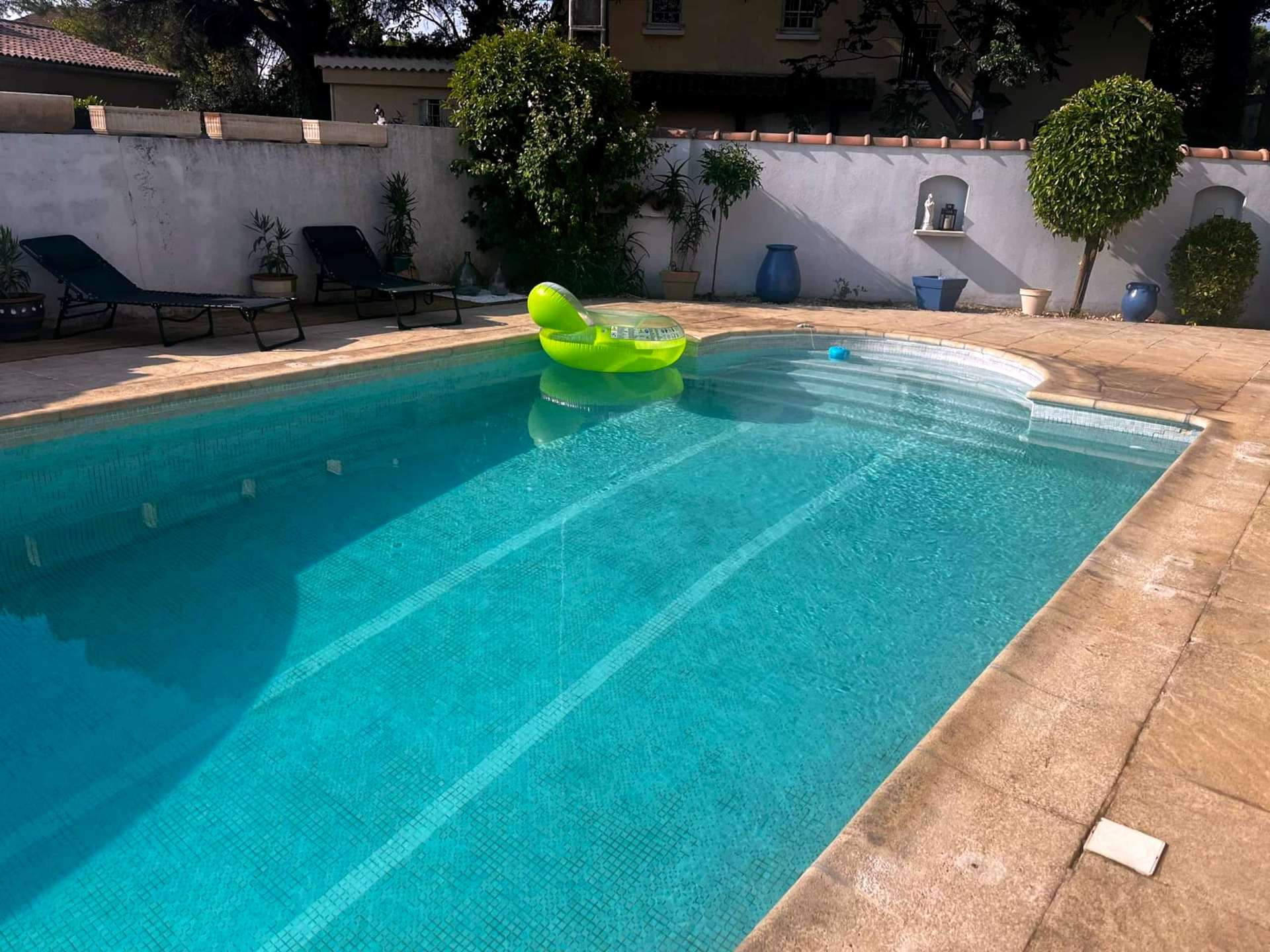 La piscine et le jardin clos, vus depuis la terrasse : bassin, transats et mur bordé d'arbustes taillés.